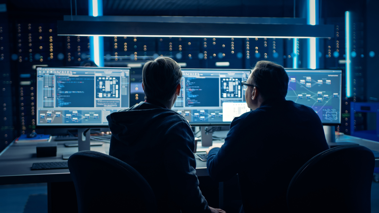Deux techniciens de dos travaillant sur les écrans d'un centre de données numériques