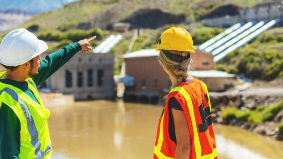 Deux ouvrier en tenues de chantier devant des grosses canalisations d'entreprise