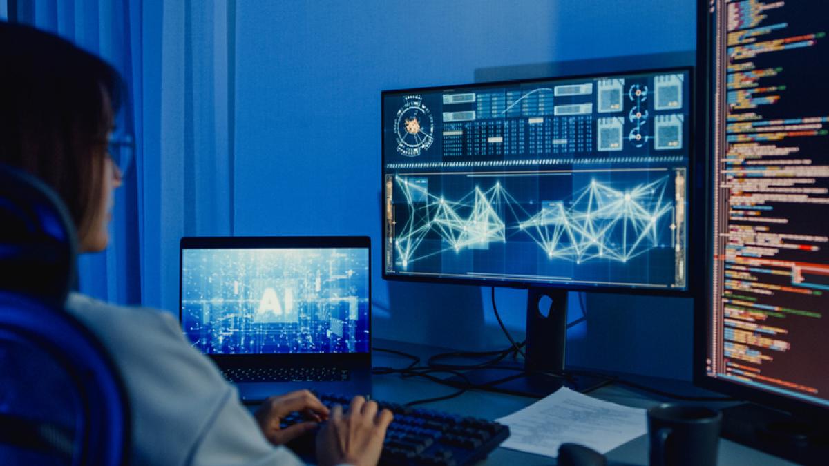 Une femme devant des ordinateurs mentionnant l'usage de l'intelligence artificielle