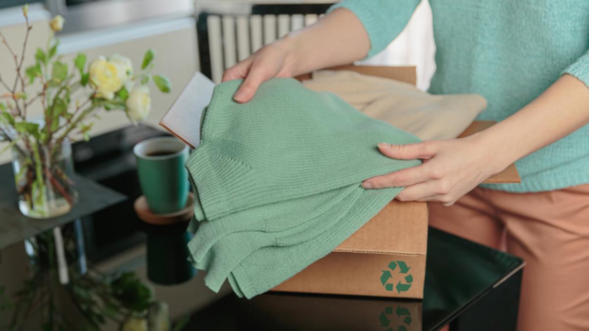 Vêtements de seconde main glissés dans un carton arborant le symbole recyclage