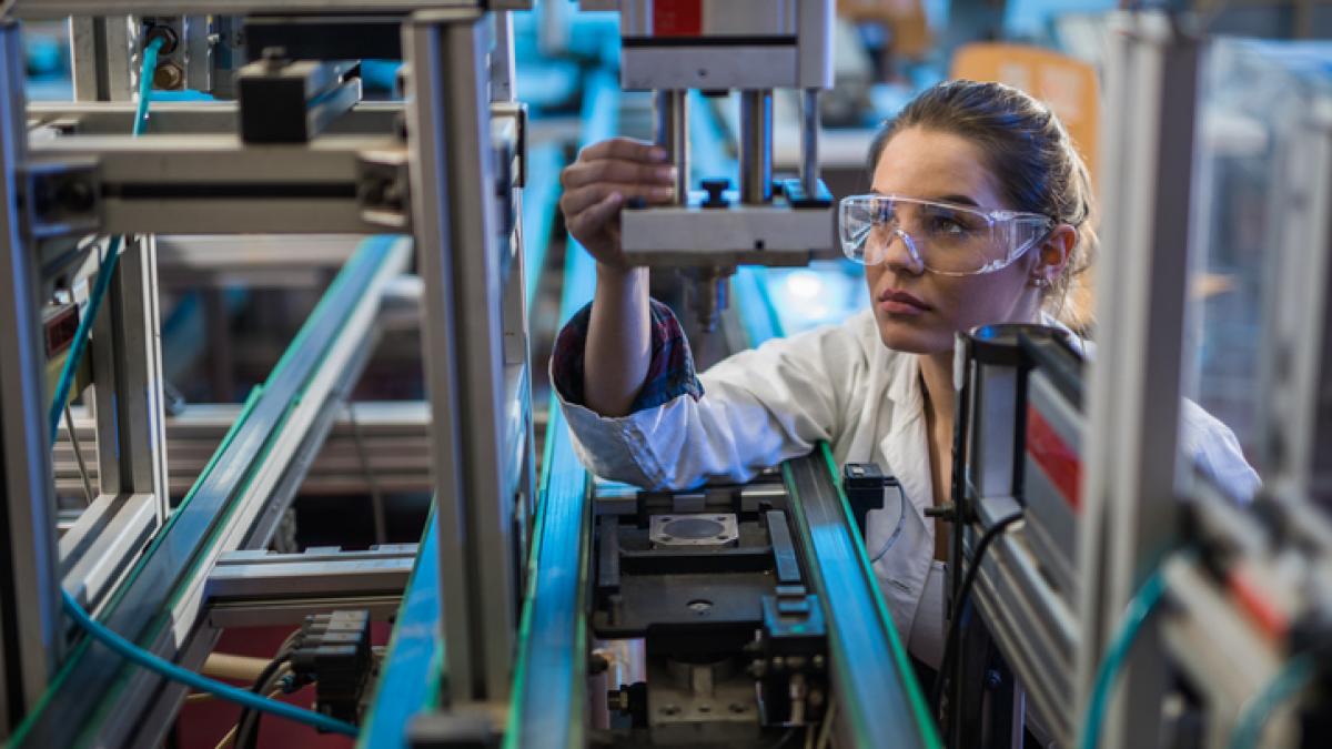 photo illustrative : femme devant une machine industrielle, lunettes de protections sur le nez