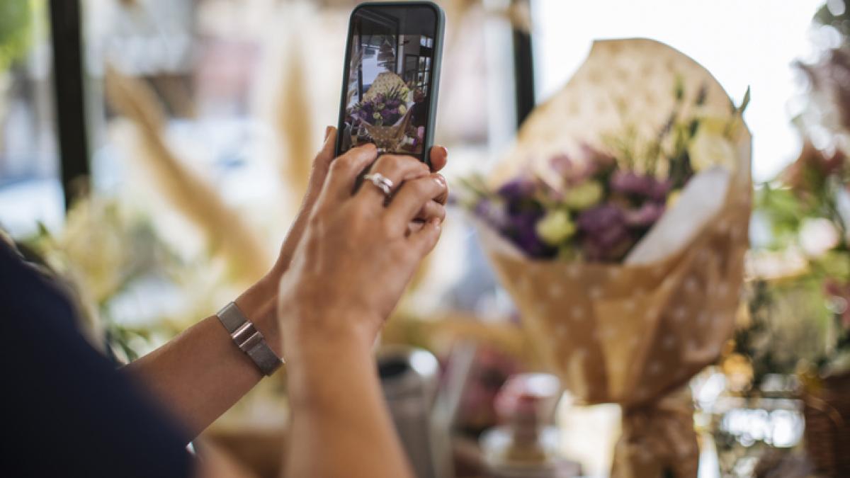 un smartphone dans les mains d'une femme, photographiant un bouquet de fleurs dans une boutique