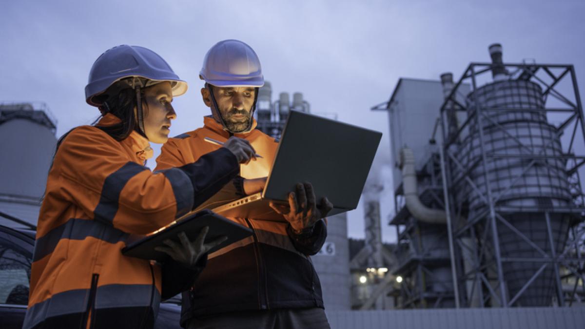 un homme et une femme travaillent de nuit sur un ordinateur face à une industrie manufacturière